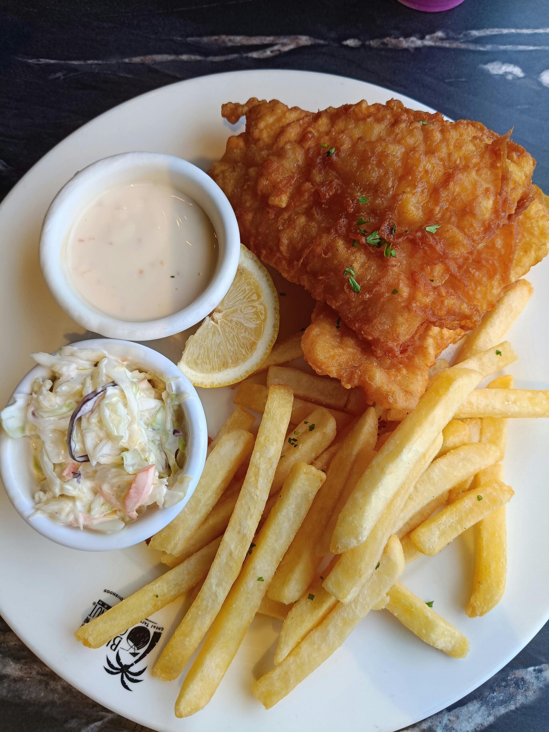 Classic fish and chips served with coleslaw and tartar sauce on a plate.